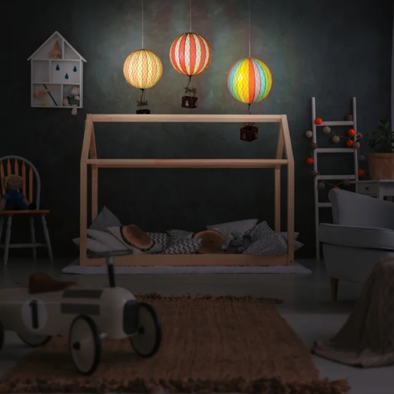 Leuchtende Deko Heissluftballone in weiss mit sanften Rosa Streifen und mit Korb aus geflochtenem Rattan von Authentic Model, die über Kinderbett hängen.