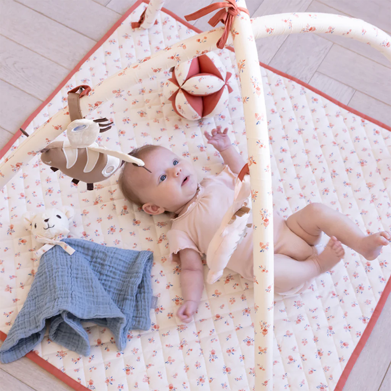 Baby spielt unter dem Spielbogen mit dem Cam Cam Copenhagen Kuschelbär in Florentine Blue.