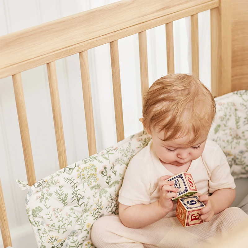 Baby spielt im Bett mit Bettnestchen mit Blumenmuster. 