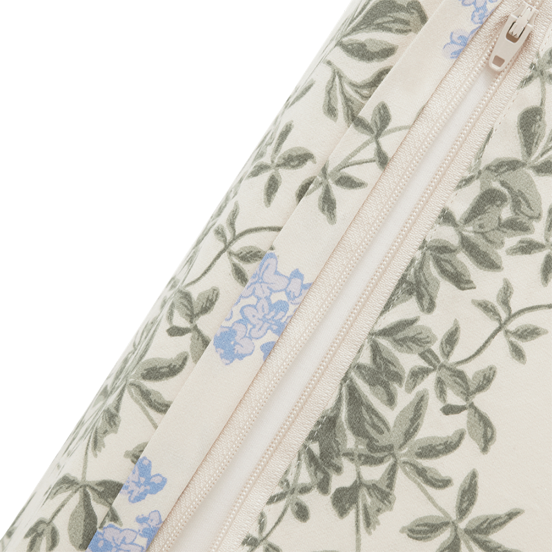 Nahaufnahme vom Muster und dem Reissverschluss des Wickelkissen in Beige mit blauen Blumen und grünen Blättern von Garbo&Friends.