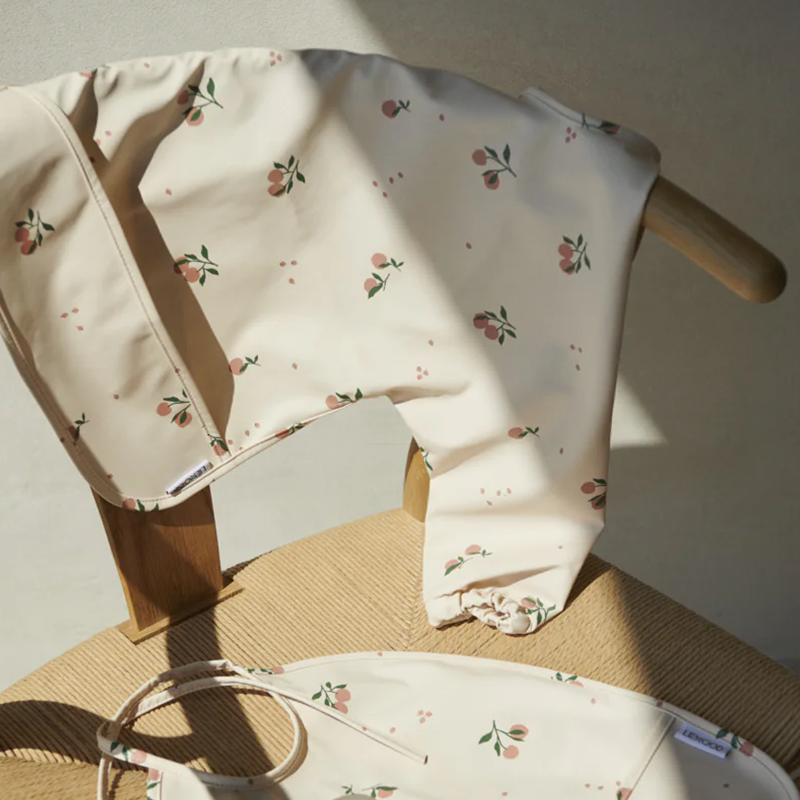 Langarmlätzchen für Kinder in Beige mit Pfirsichmuster von Liewood auf einem Stuhl.