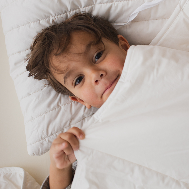 Junge liegt auf weissem Kissen  und unter einer Bettdecke für Kinder von Murmunto in Weiss. 