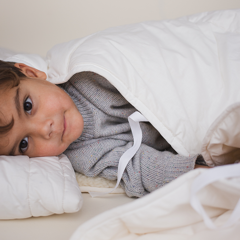 Junge liegt auf der Seite auf weissem Kissen  und unter einer Bettdecke für Kinder von Murmunto in Weiss. 