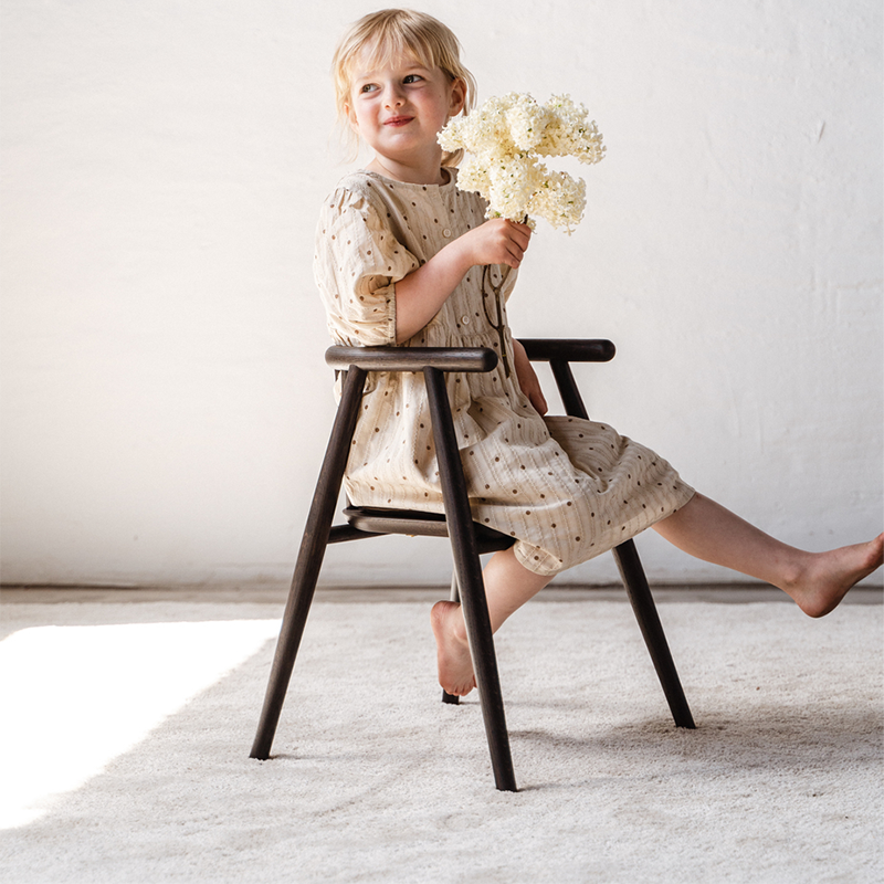 Mädchen sitzt auf dem Oaklings Kinderstuhl 'Storm' in Smoked Oak. 