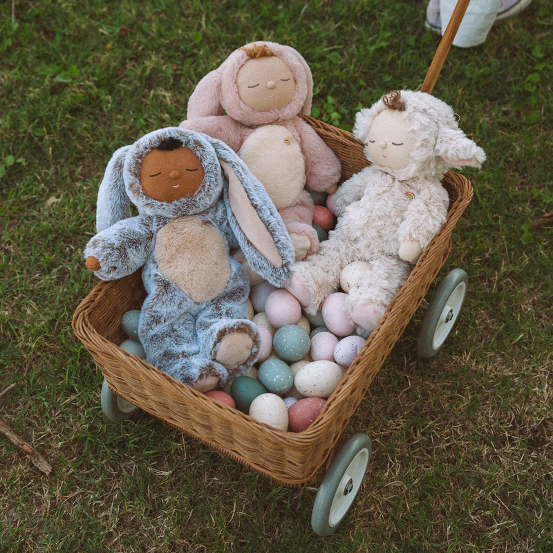 Flauschige Puppen im Hasenanzug sitzen auf bunten Ostereiern in einem Leiterwagen.