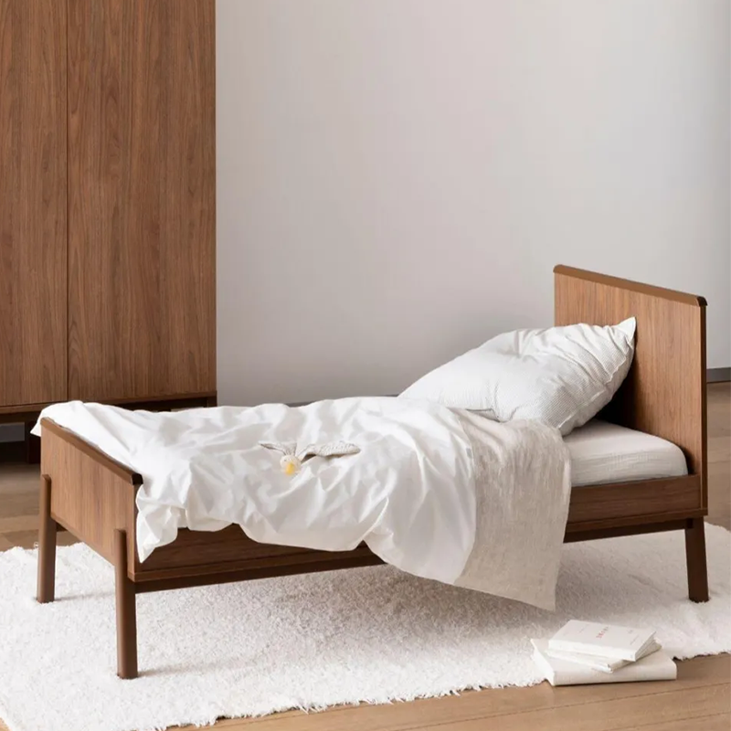 Juniorbett in Kastanienbraun ohne Matratze von Quax steht in einem Kinderzimmer auf einem weissen Teppich. Im Hintergrund steht eine Kommode und ein Schrank.