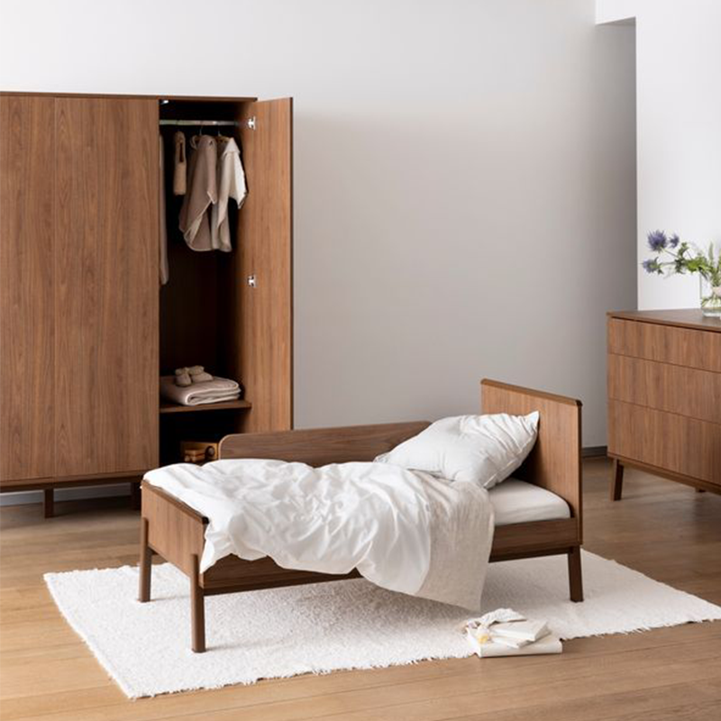 Dreitüriger Schrank in Kastanienbraun von Quax in einem Kinderzimmer. Vor dem Schrank steht ein Kinderbett.