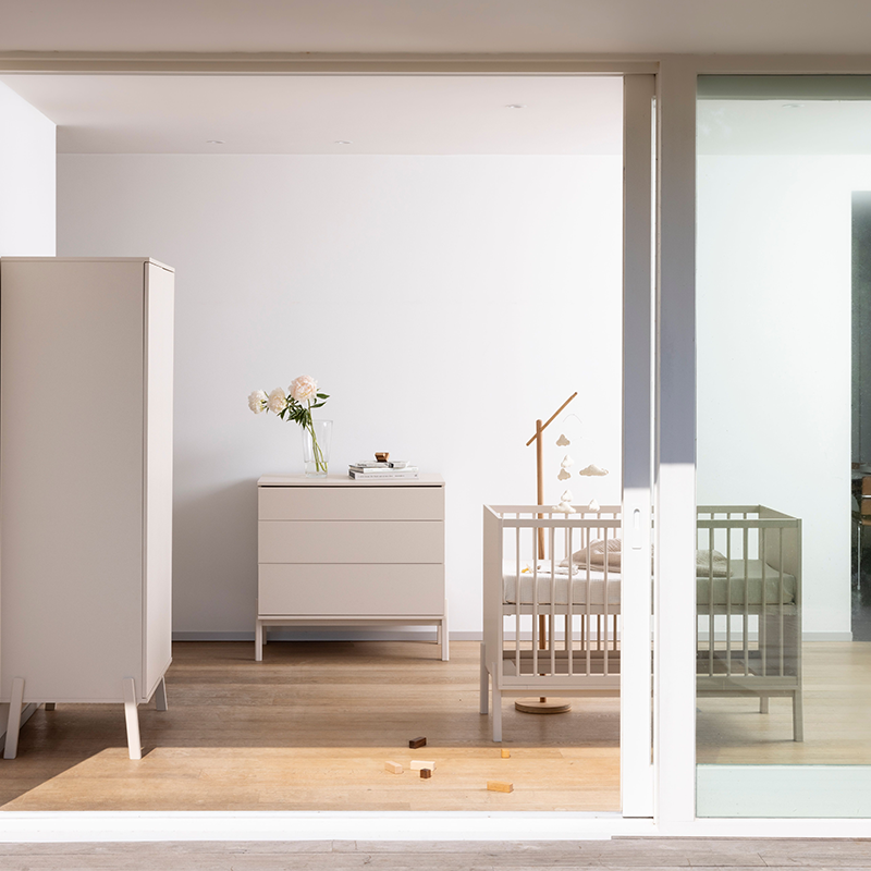 Blick ins Kinderzimmer mit einem Schrank, einenr Kommode und einem Babybett alles in einer hellen Lehmfarbe von Quax.