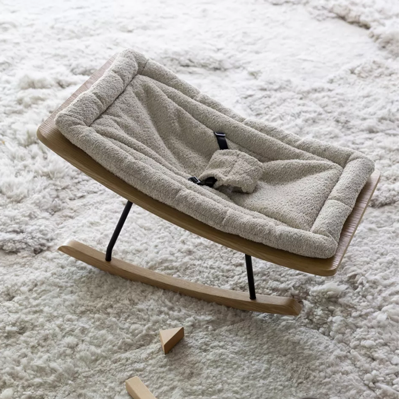 Babywippe mit Holzkufen und beiger Bouclé-Stoff Polsterung von Quax auf weissem Teppich.
