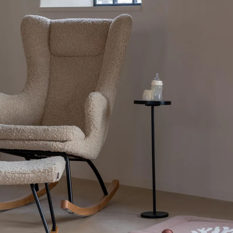 Beistelltisch mit runder Tischplatte in Schwarz von Quax. Neben dem Tisch befindet sich ein beiger Schaukelstuhl und auf dem Tisch ein Babyfläschchen.