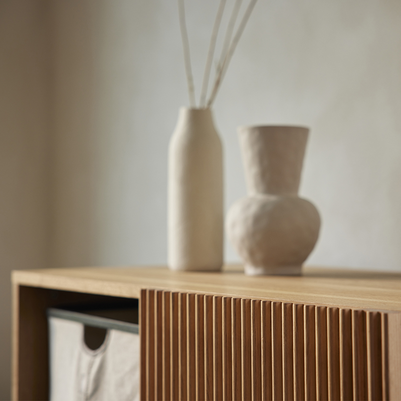 Nahaufnahme von Kommode aus Ahornholz mit vier Ablagefächern und elegante Schiebetür mit Gitterstäben von Quax. Auf 2 Ablagefächern stehen Aufbewahrungskörbe und auf der Kommode stehen 2 beige Vasen.