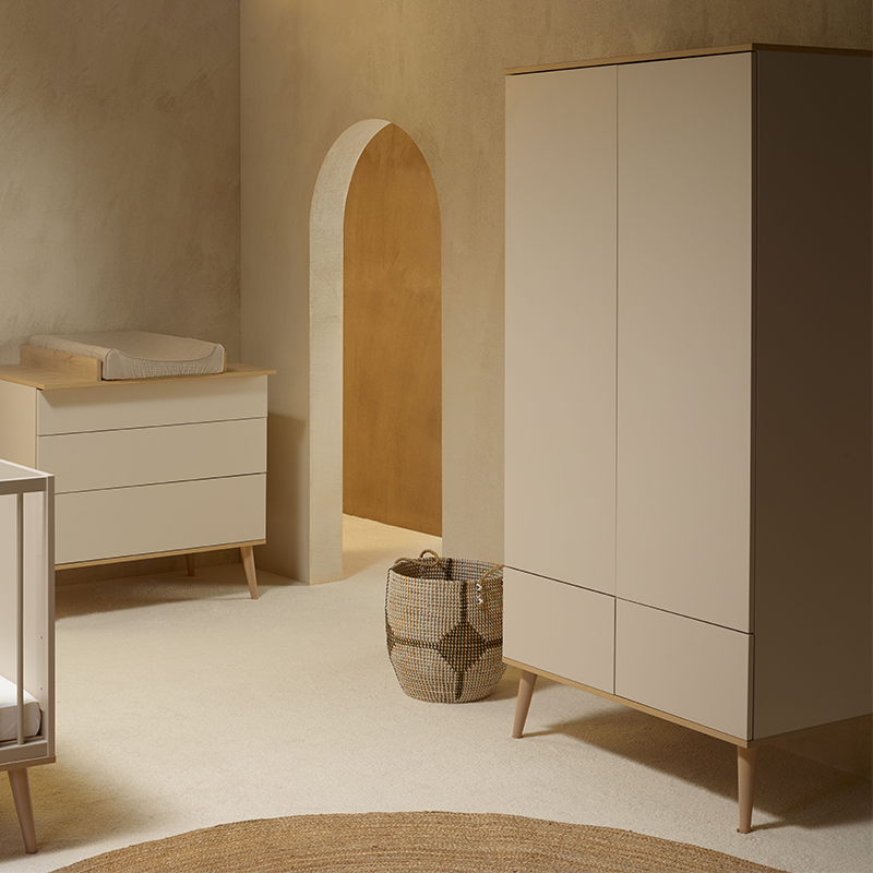 Zweitüriger Schrank mit 2 Schubladen in grau-beige mit Beinen aus massiver Buche von Quax in Kinderzimmer mit Wickelkommode auf der anderen Seite.