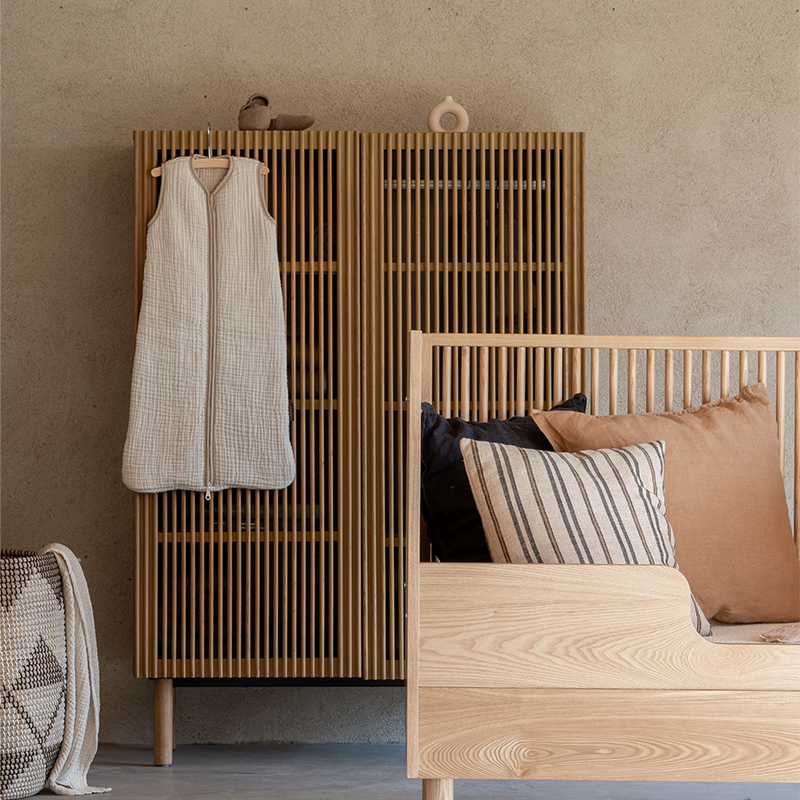 Eichenschrank mit zwei Türen von Quax steht hinter Bett in Kinderzimmer. An der Tür hängt ein Baby Schlafsack.