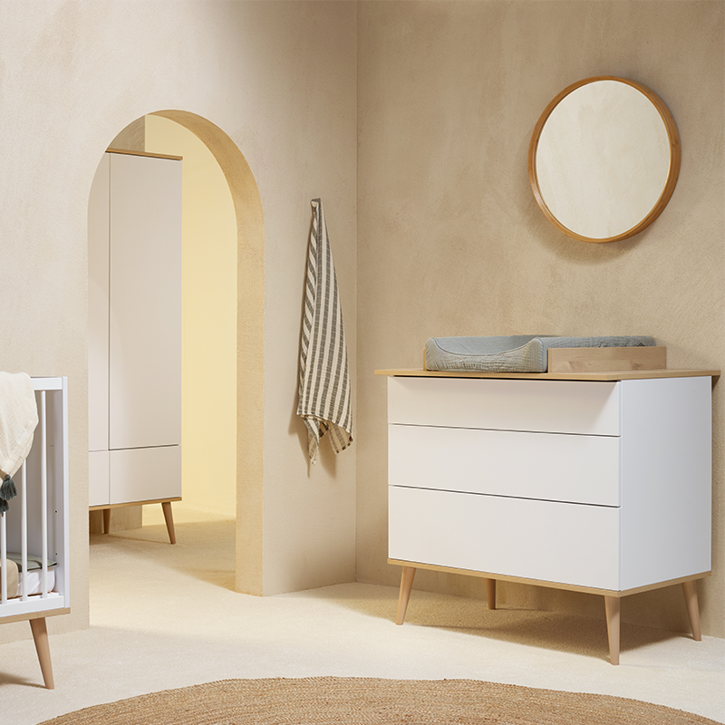 Wickelkommode in Weiss mit 3 geräumigen Schubladen mit Wickelaufsatz aus Buchenholz und Beinen aus Buchenholz von Quax steht in einem Kinderzimmer. Oberhalb der Kommode ist ein Spiegel.