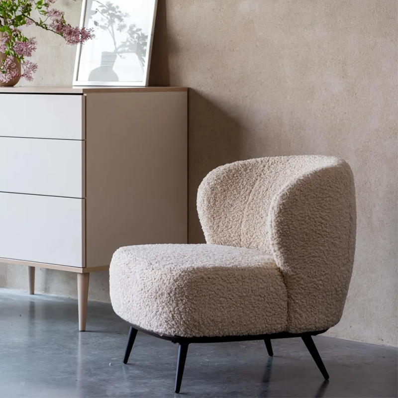Loungesessel in Beige mit weichem Teddy-Bezug von Quax steht neben einer weissen Kommode. 