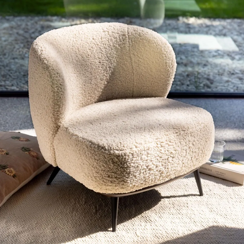 Loungesessel in Beige mit weichem Teddy-Bezug von Quax steht auf einem Teppich vor einem Fenster.