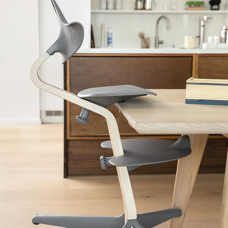 Nomi Hochstuhl für Kinder mit Mittelbalken aus Holz und Sitz, Rückenlehne  und Fussauflage und Füsse in grauem Plastik von Stokke auf Tisch aufgestuhlt. 