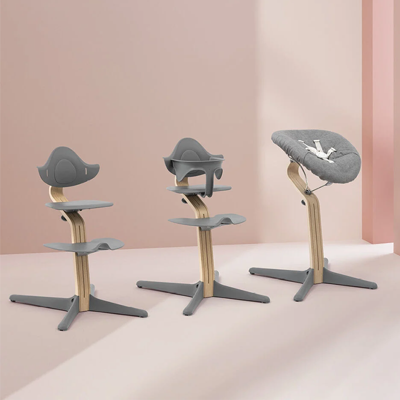 Nomi Hochstuhl für Kinder mit Mittelbalken aus Holz und Sitz, Rückenlehne  und Fussauflage und Füsse in grauem Plastik von Stokke mit Kindersitz, Kleinkindersitz und Babyauflage. 