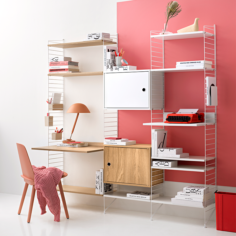 Regalsystem von String mit weissen Regaleitern und einer Tischplatte in Eiche, Regalböden in Eiche und Weiss und Schrankelementen in Weiss und Eiche mit 3 Aufbewahrungsboxen in verschiedenen Grössen in Beige, die an der Seite des Regals hängen.