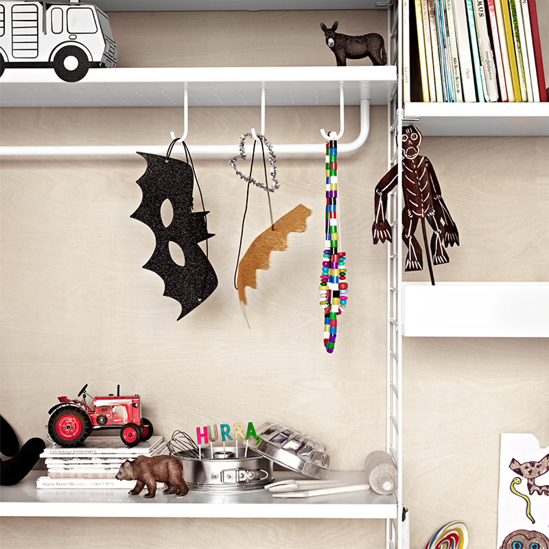 String Furniture Regal in Weiss mit Haken an denen Kindermasken und Ketten hängen.