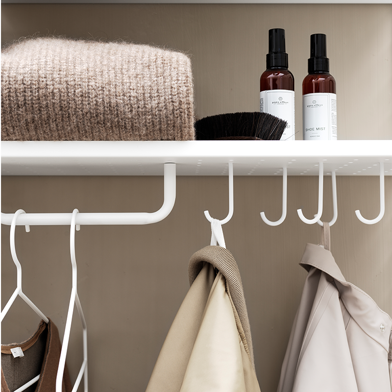 Regalboden von String mit Haken in Weiss an denen Jacken hängen.