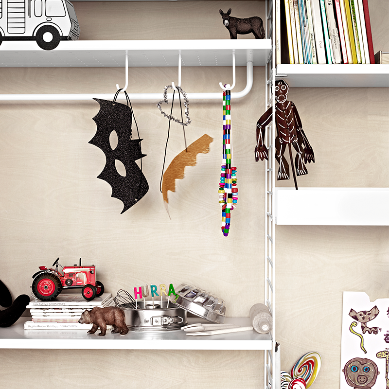 String Furniture Regalsystem in Weiss für Kinder mit Regalboden mit Haken an denen Kindermasken und Ketten hängen. 