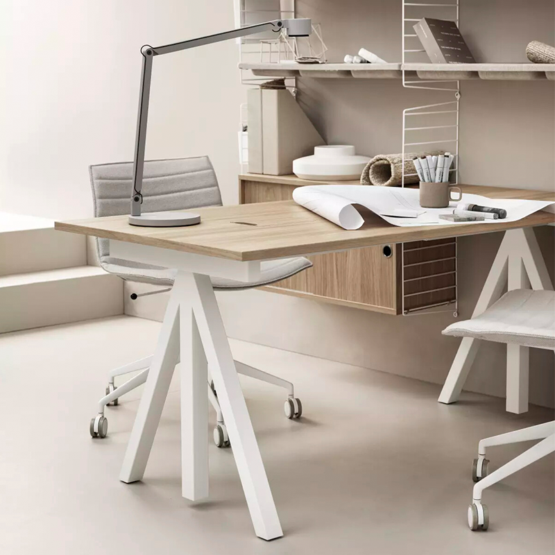 Schreibtisch mit Tischplatte aus Eiche und Tischbeine in Weiss von String Furniture. Steht neben einem String Regal.