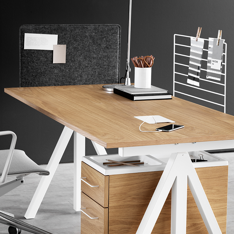 Schreibtisch mit Tischplatte aus Eiche und Tischbeine in Weiss von String Furniture mit Handy, Stiftebecher und Bücher drauf. Unter dem Tisch steht ein Schubladensystem. 