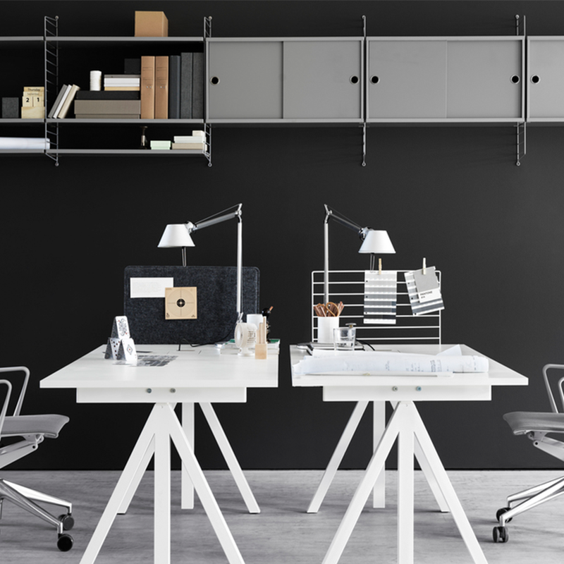 2 höhenverstellbare Schreibtische mit Tischplatte aus Eiche und Tischbeine in Weiss von String Furniture mit Schreibtischlampe und Büroutensilien auf den Tischen. 