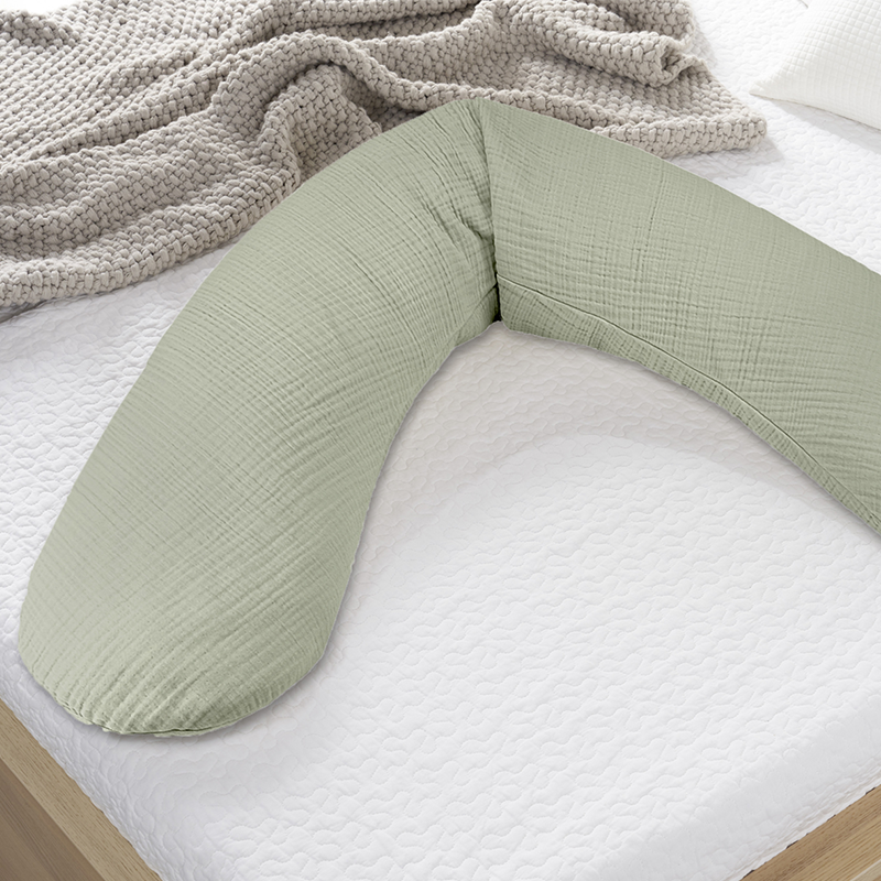 Still- und Schwangerschaftskissen in Salbei aus Musselin von Theraline liegt auf einem Bett.