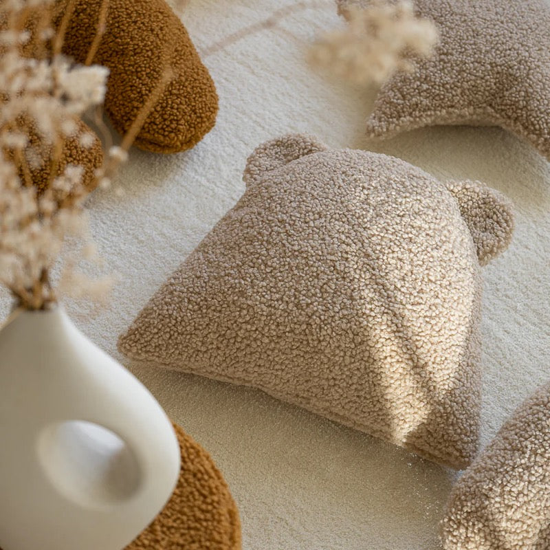 Kuscheliges Bärenkissen in beige zwischen anderen Dekokissen aus Teddy-Stoff. Alles in den schönsten Natur-Farbtönen