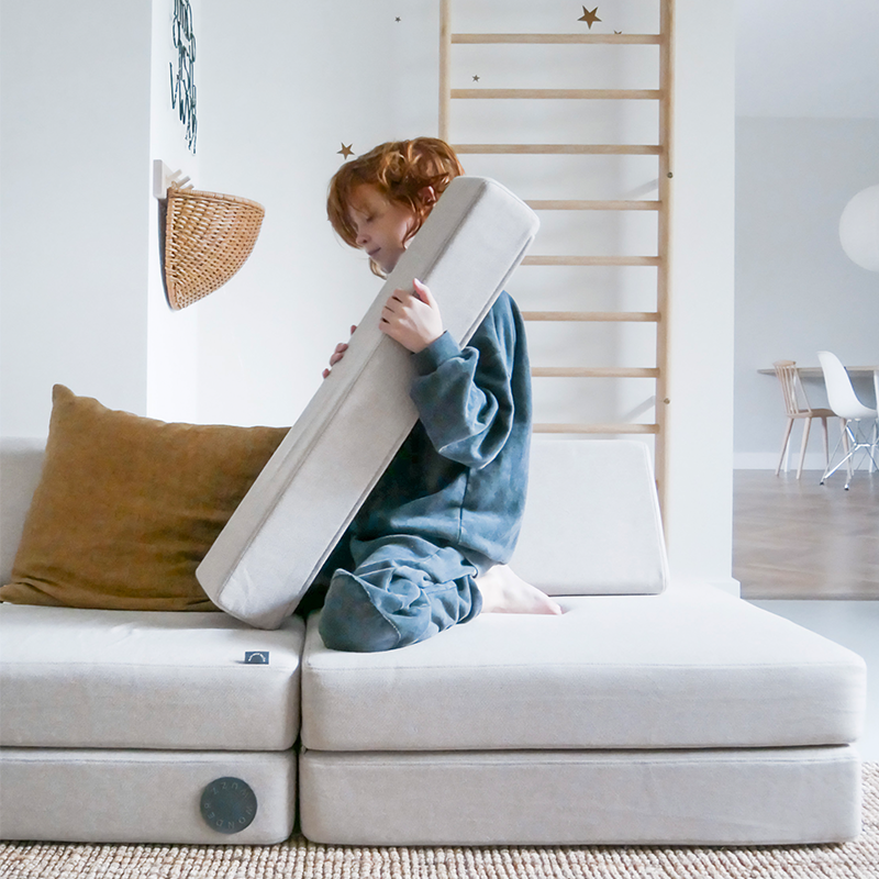 Wonderwuzz modulares Spielsofa 'OH SO SOFY' in der Farbe Grauffelo mit Kind, das auf dem Sofa spielt. 