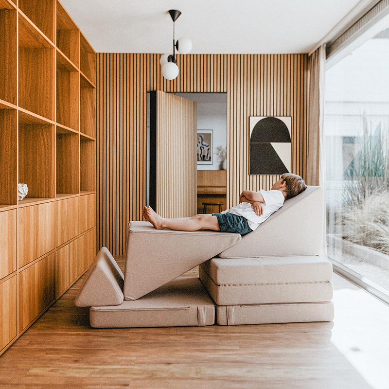 Junge der auf dem Wonderwuzz Spielsofa mit 8 modularen Teilen 'Oh so sofy' in der Farbe Beigemarie liegt. 