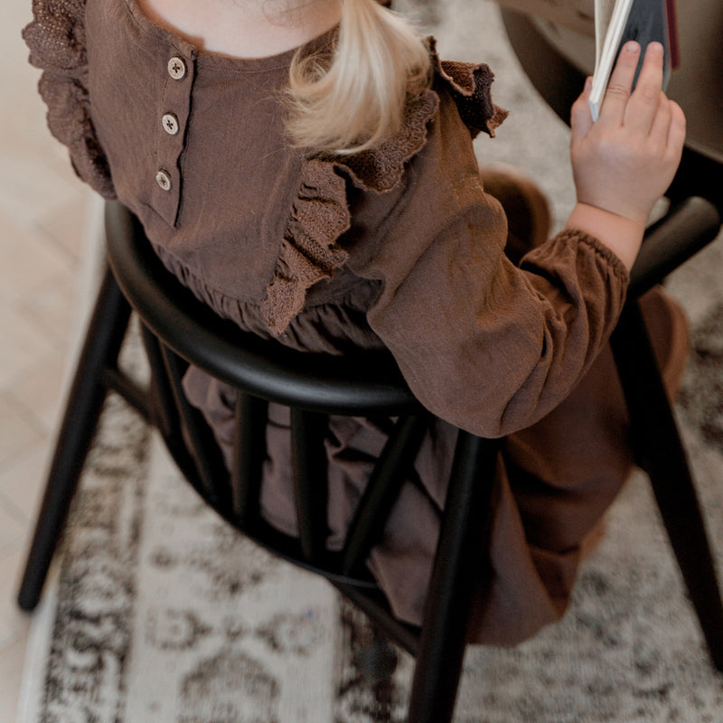 Mädchen sitzt auf dem Oaklings Kinderstuhl 'STORM' in Smoked Oak. 